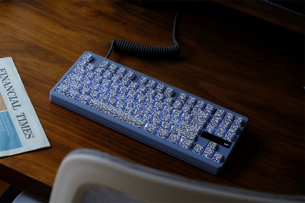 Mechanical keyboard with a coiled cable on a wooden desk with White Ink Swirl Side Engraved Keycaps on it
